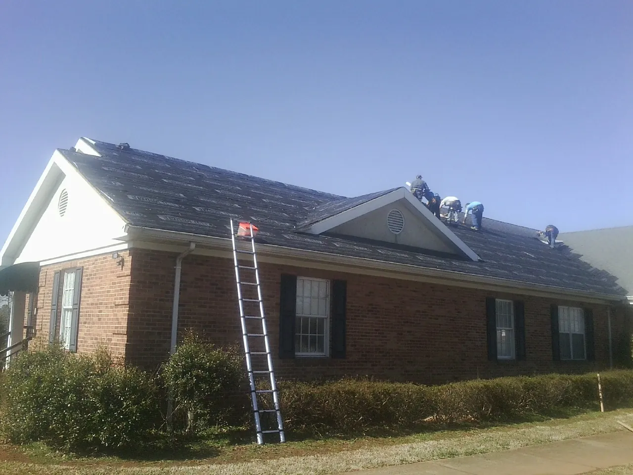 Crew tearing shingles off a brick ranch roof with a ladder set — Metal Roof Repair work by our crew in Stewartstown
