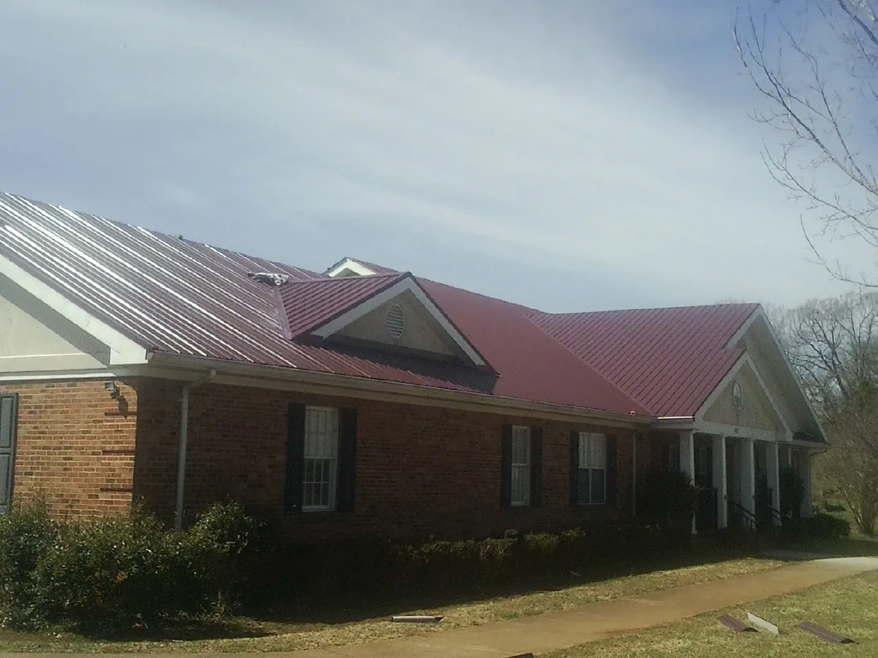 Red metal roof with gabled entries on a long brick building, from a Hail Damage Roof Repair job in Stewartstown