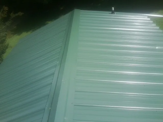 New green metal panels meeting at the ridge of a roof — Flat Roof Repair work by our crew in Stewartstown