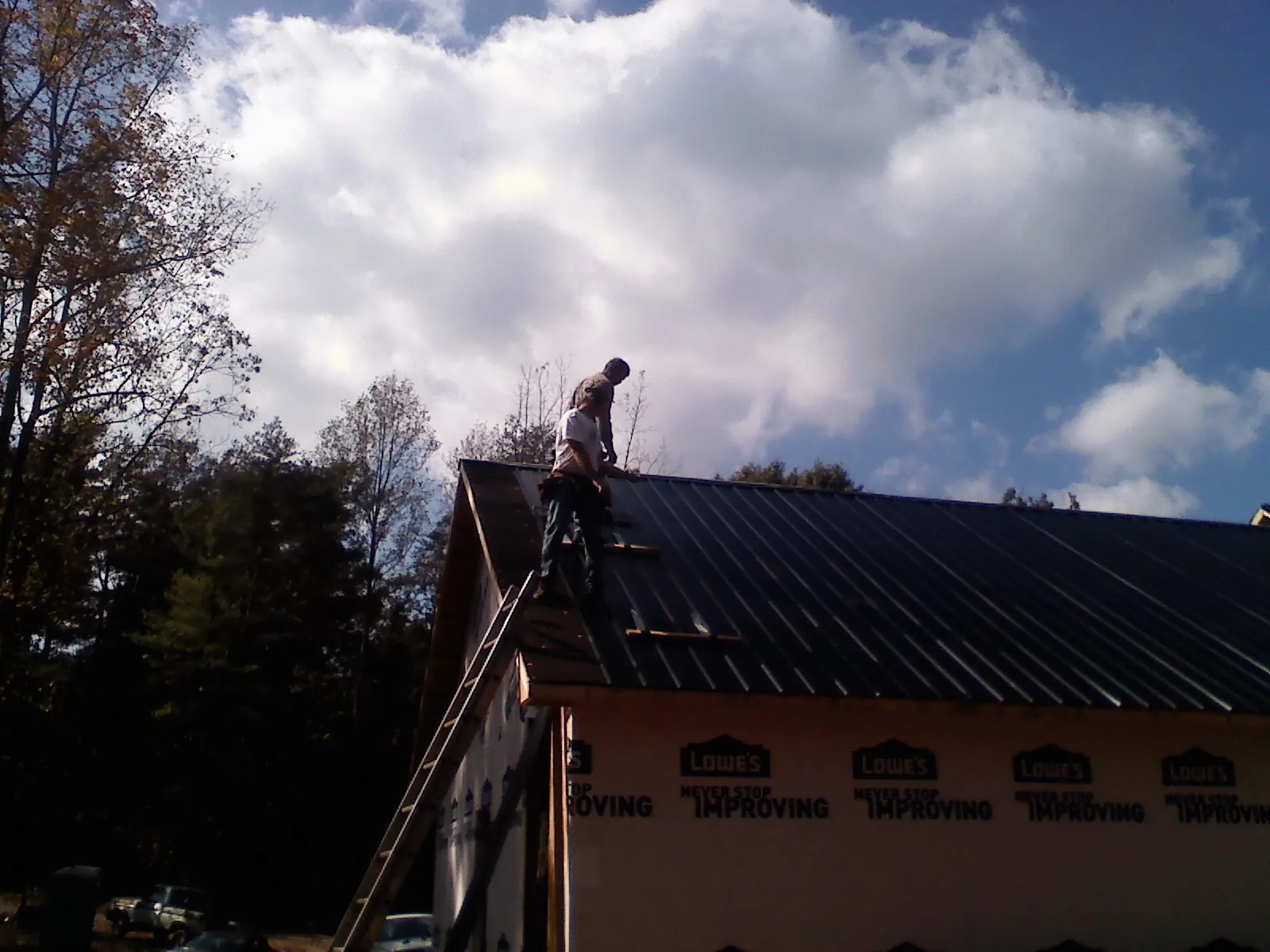 Roofer fastening dark metal panels high against a cloudy sky, from a Roof Inspection job in Stewartstown
