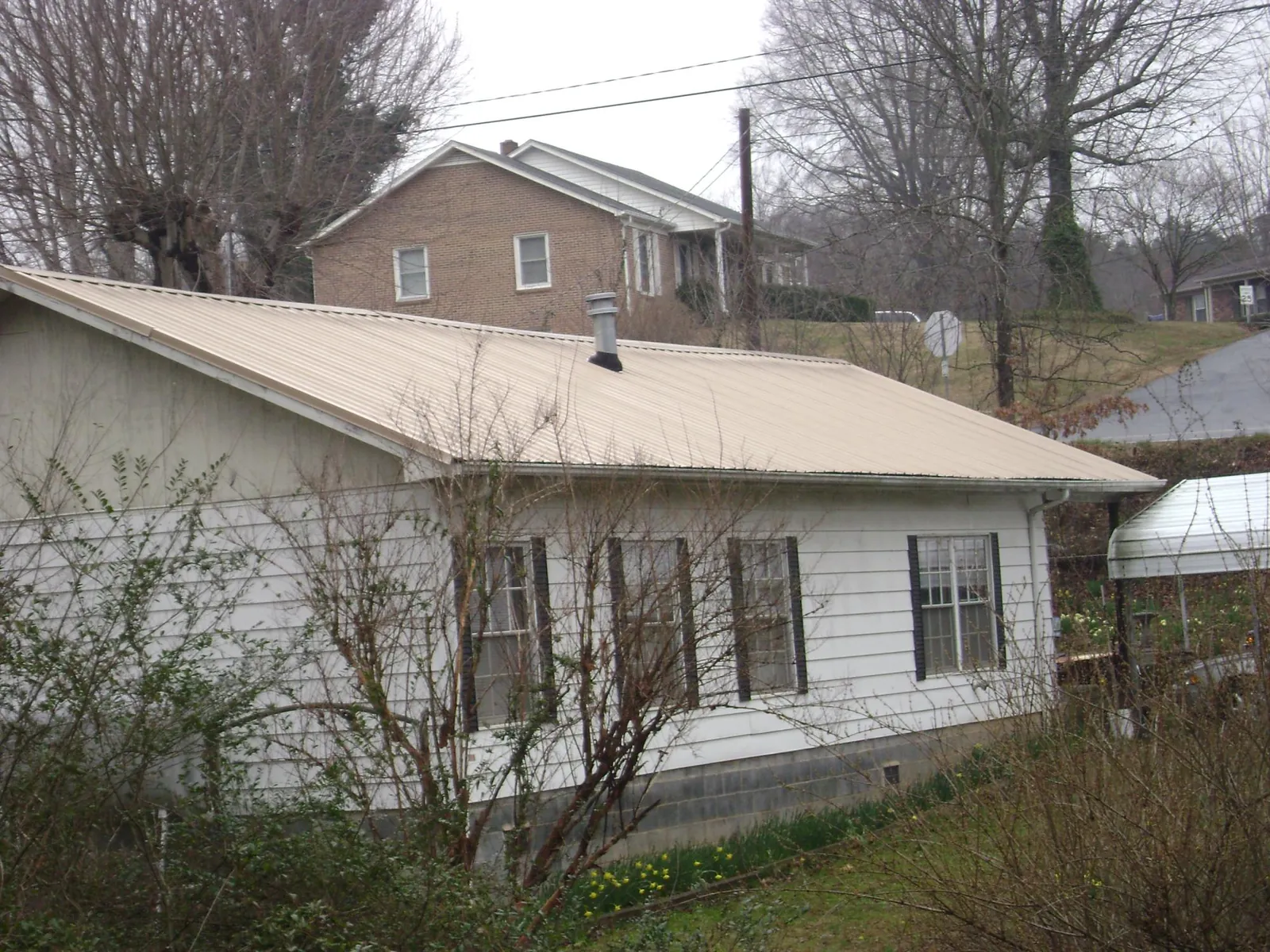 Tan metal roof on a white sided house set into a hillside — Commercial Roofing by Roofing Brothers in Stewartstown